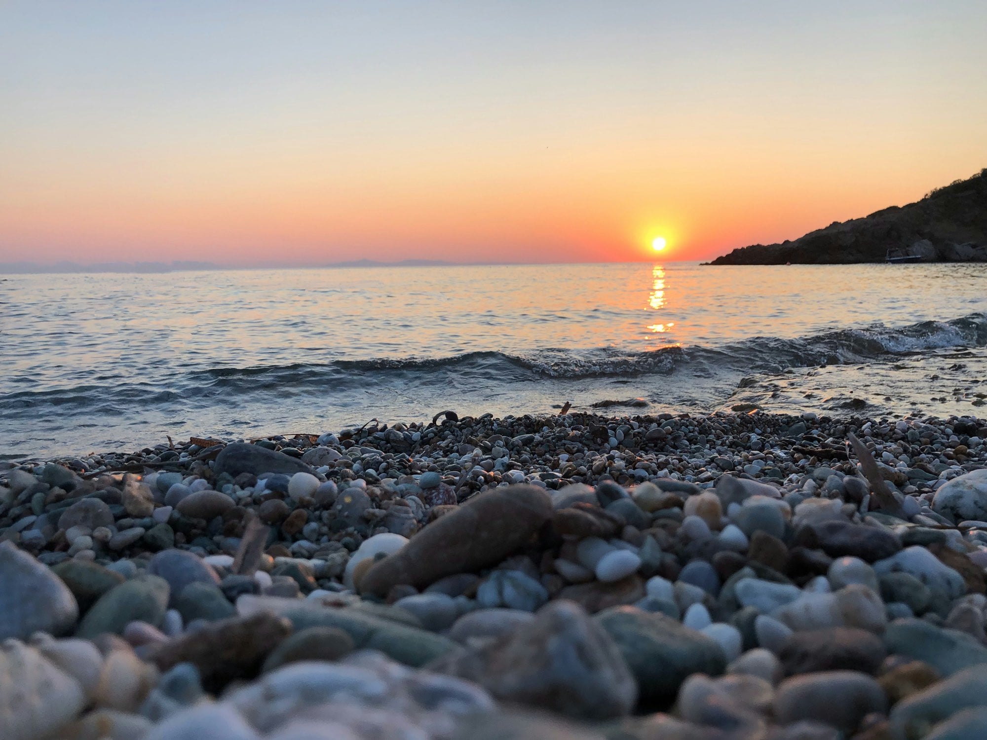 The sun dropping into the sea over the pebbled shoreline of the Athens Riviera, a short ride from the centre of the city.