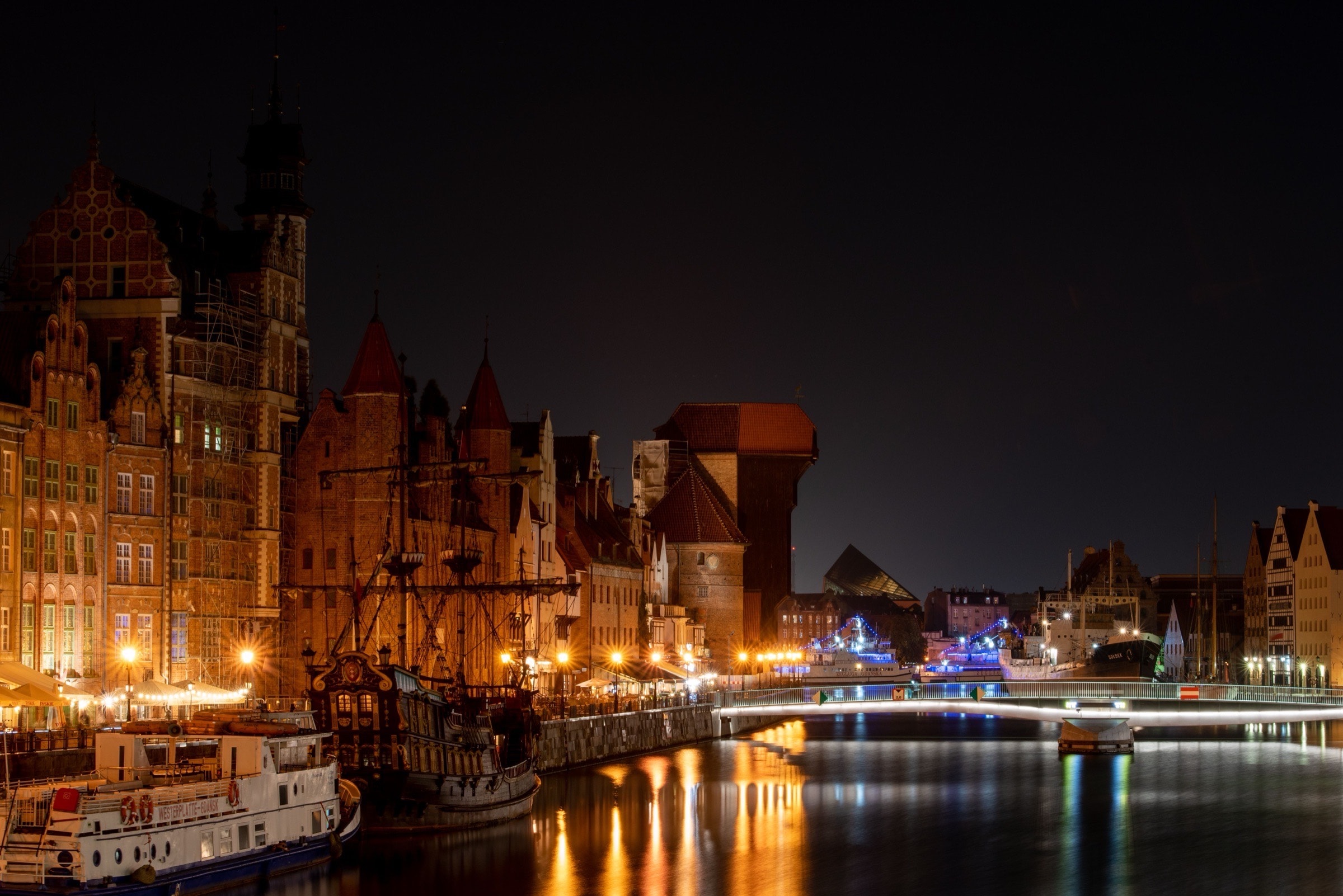 The lamplit Motława waterfront at night — masts, brick gables and the Crane